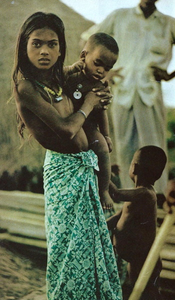 A village girl near Chiringa, Bangladesh carries a smaller child while her mother cooks and sews
National Geographic | September 1972