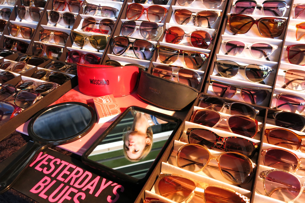 A woman's reflection in a mirror amidst a sea of sunglasses.
